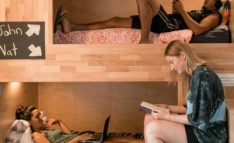 people hanging out in hostel dorm room with pod style beds